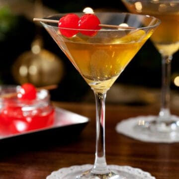 A martini served with maraschino cherries in front of a Christmas tree