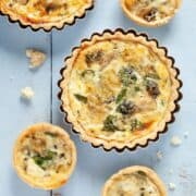 Overhead view of Blue Cheese, watercress and artichoke tarts. A large tart in in it's baking tin, smaller tarts on on the worktop