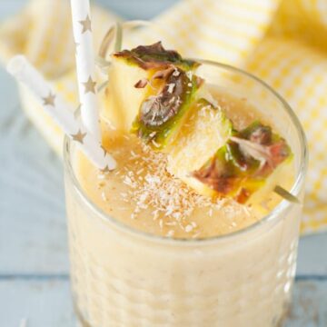 Pineapple coconut cold busting smoothie with chunks of fresh pineapple, dessicated coconut and paper straws garnishing this yellow drink