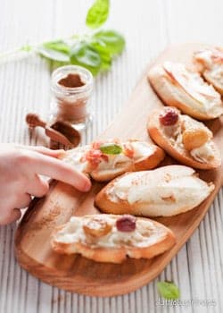 A platter of mixed taleggio crostini with a person taking one