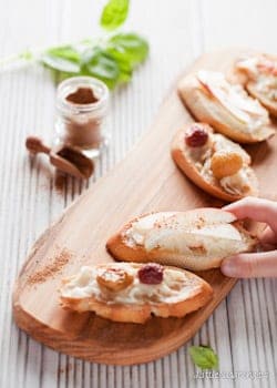 A platter of mixed taleggio crostini with a person removing one