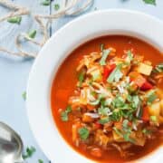 Red Mulligatwany soup in a white bowl. The corner of the bowl is just out of shot. Fresh coriander garnishes the soup