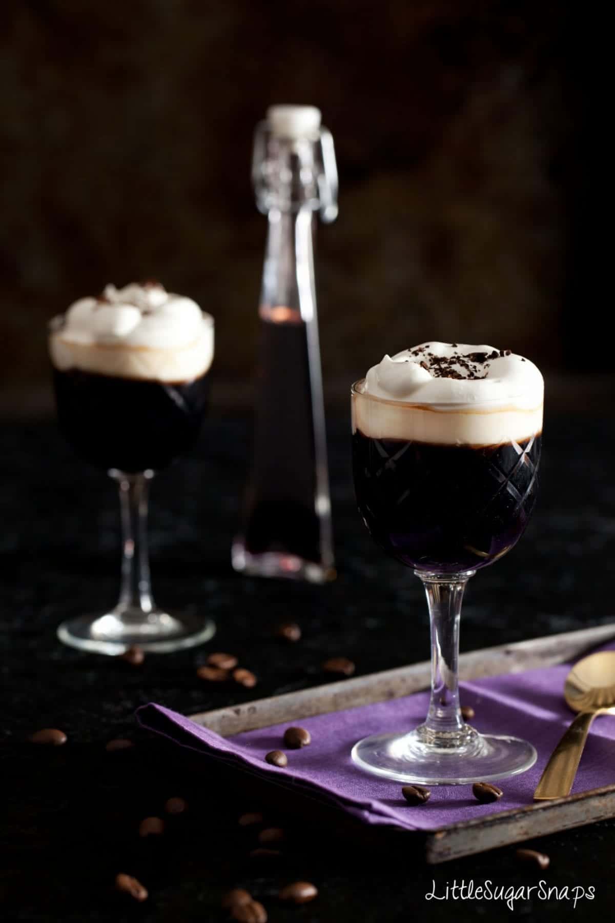 Coffee drinks topped with whipped cream with blackcurrant liqueur bottle behind
