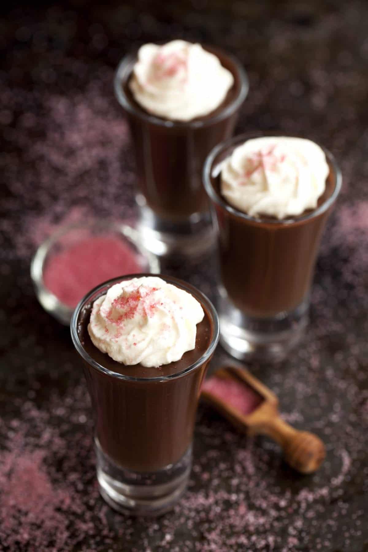 Three small glasses of chocolate dessert topped with whipped cream