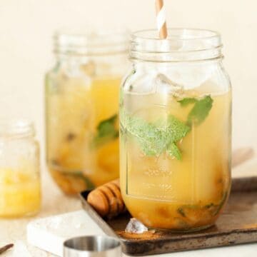 A blend of bourbon, pear, pineapple, mint and cinnamon drink in a jam jar with a cocktail jigger in shot