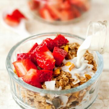 Milk being poured into a bowl of coconut and mango granola topped with chopped strawberries