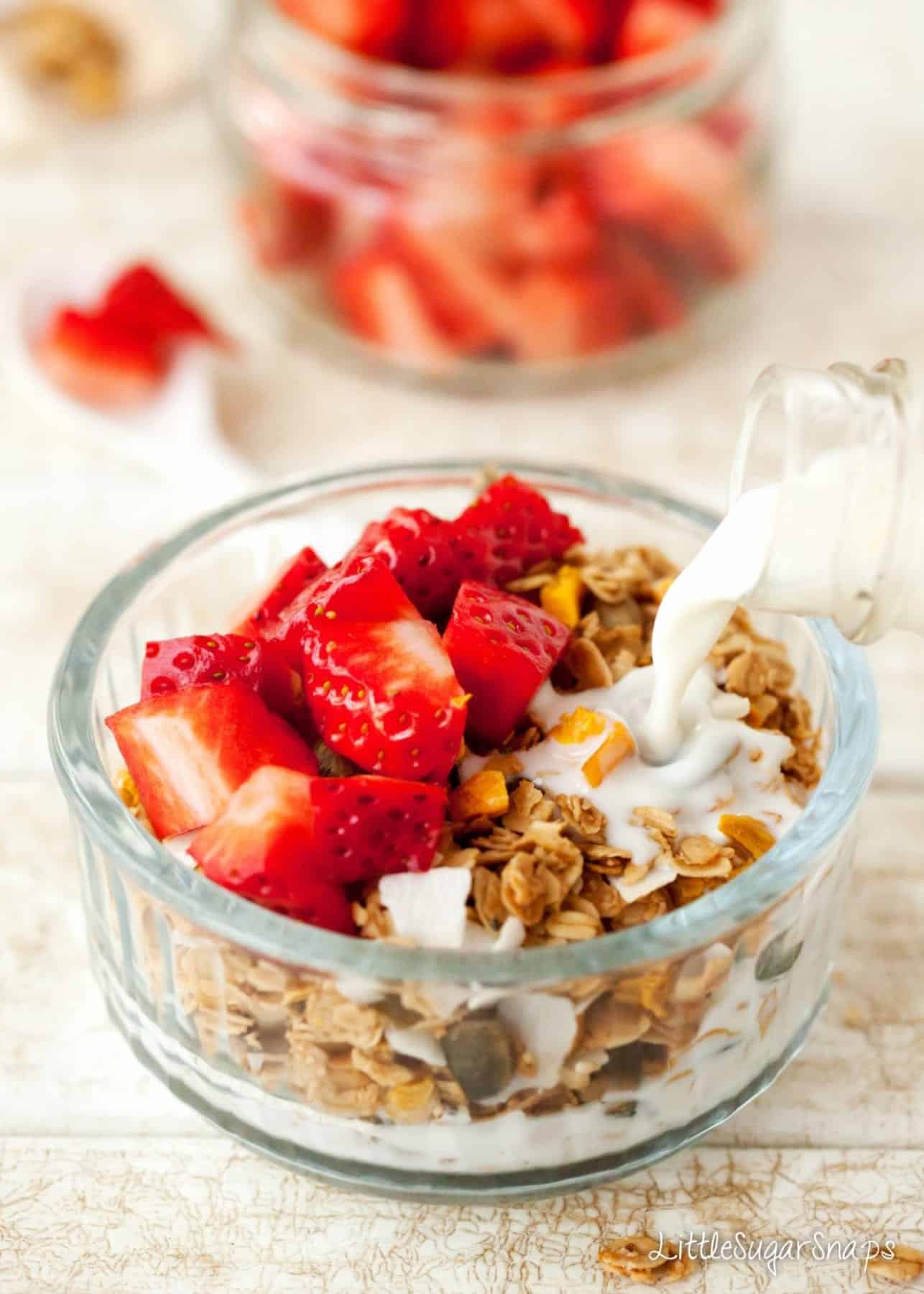 Coconut Mango Granola Milk being poured onto a bowl of granola with strawberries on top