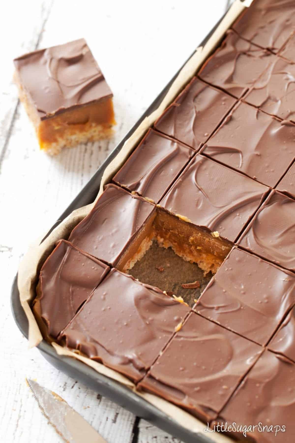 Millionaire's Caramel Krispie Squares in a baking tin. One piece is missing