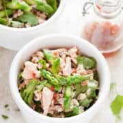 Thai Salmon & Rice Lunch Bowls with salmon, rice, asparagus and fresh herbs. A bottle of dressing is just behind the front bowl