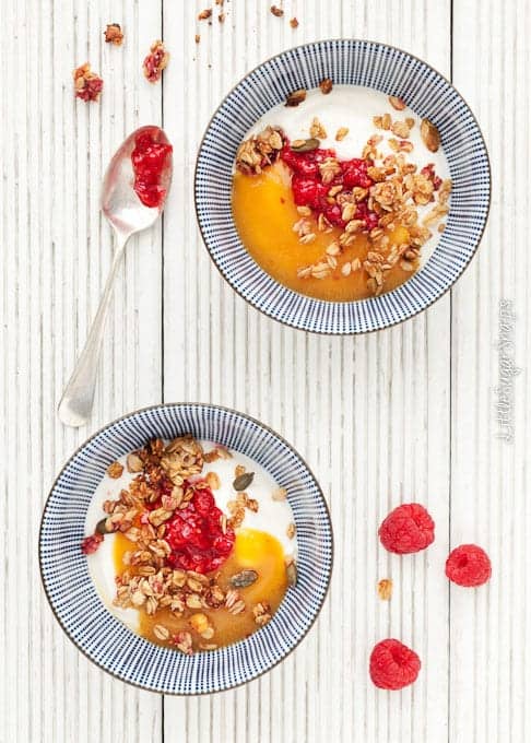 Yoghurt in bowls with peach puree, crushed raspberries and granola