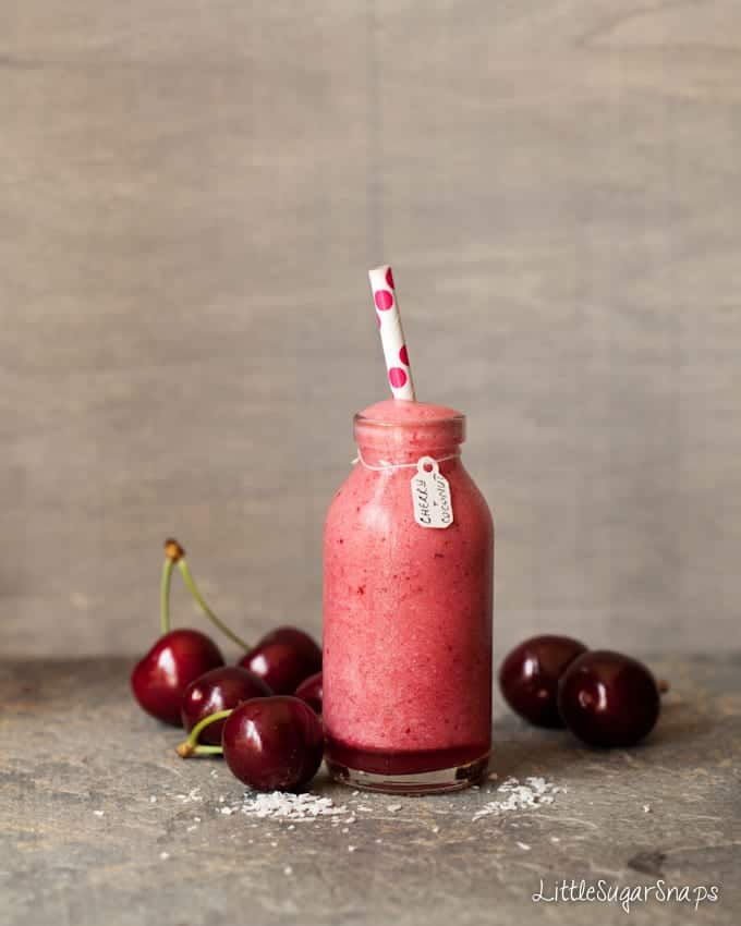 Small bottle holding Cherry Smoothie with fresh cherries alongside