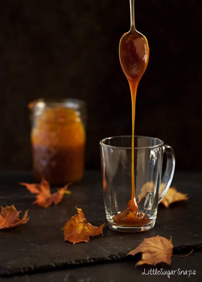 Caramel sauce dripping from a spoon into a glass mug. 