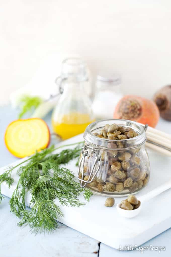 A jar of capers next to fresh dill on a wooden board