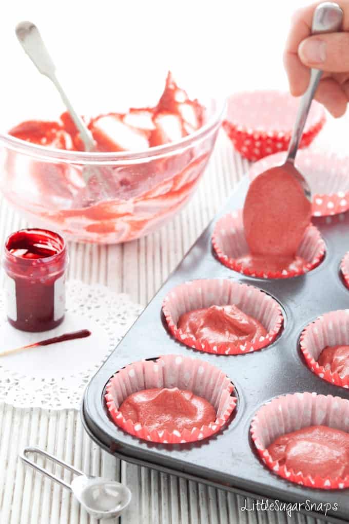 Spooning red velvet cupcake batter into baking cases