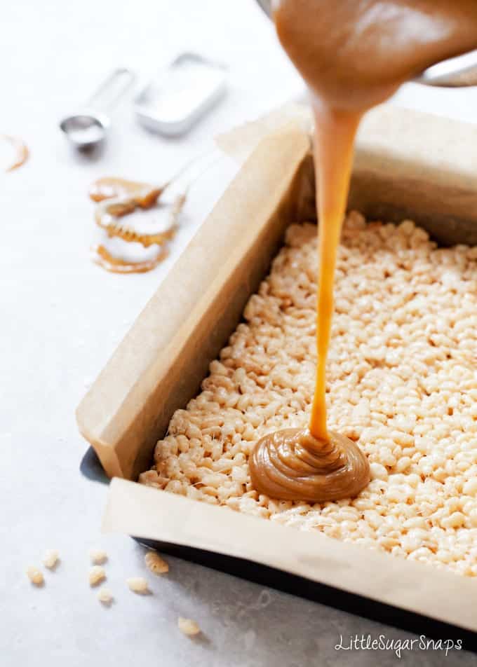 Pouring caramel over a rice krispie treats layer in a baking tin