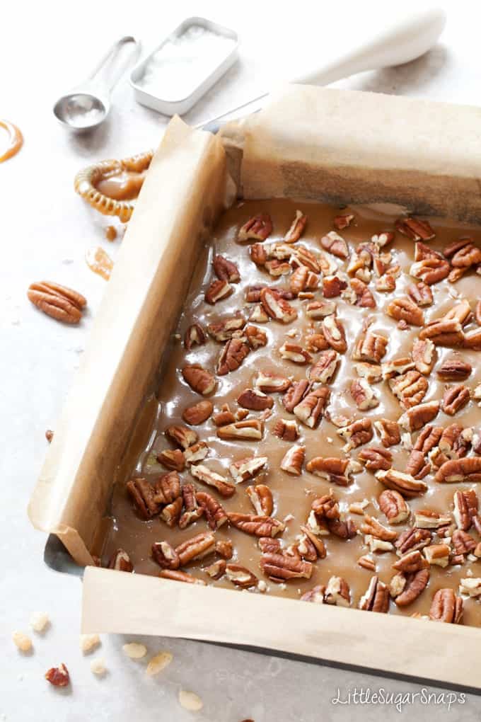 Pecan nuts sprinkled over caramel in a baking tin