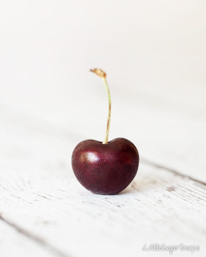 A single cherry stood upright on a tabletop