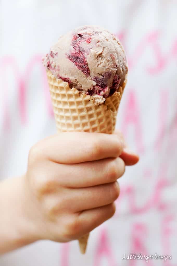 A child holding a waffle cone with chocolate and blackberry ripple ice cream