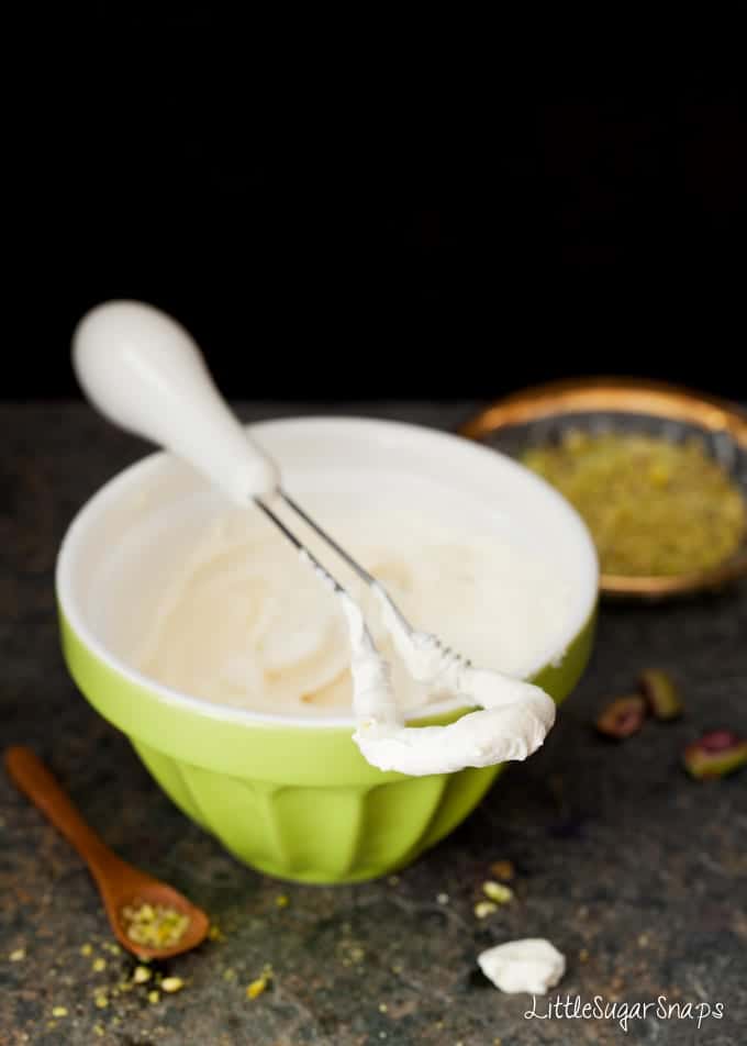 Mascarpone frosting in a green bowl with a small whisk on top.