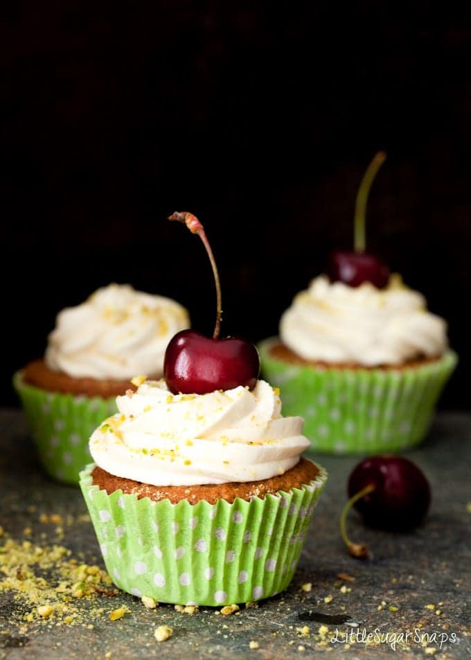 Three pistachio cupcakes decorated with mascarpone frosting and a fresh cherry