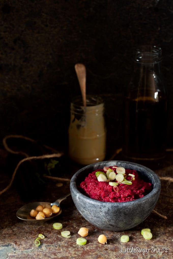 a bowl of beetroot hummus topped with spring onions.