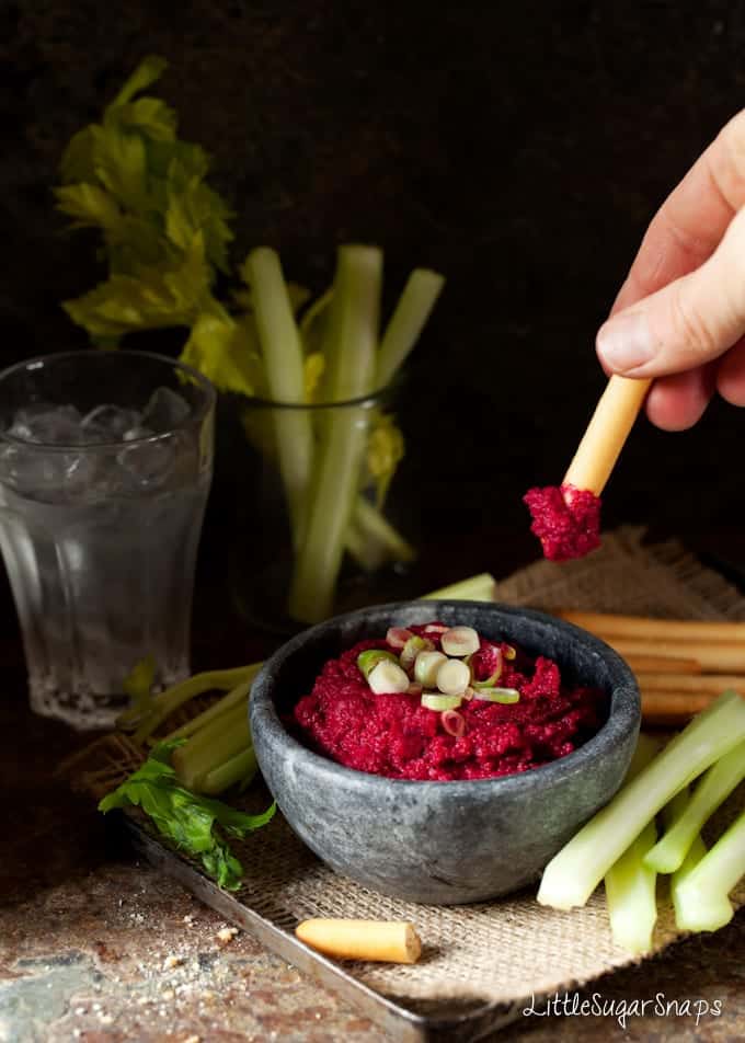 Person dipping a breadstick into a bowl of Beetroot hummous.