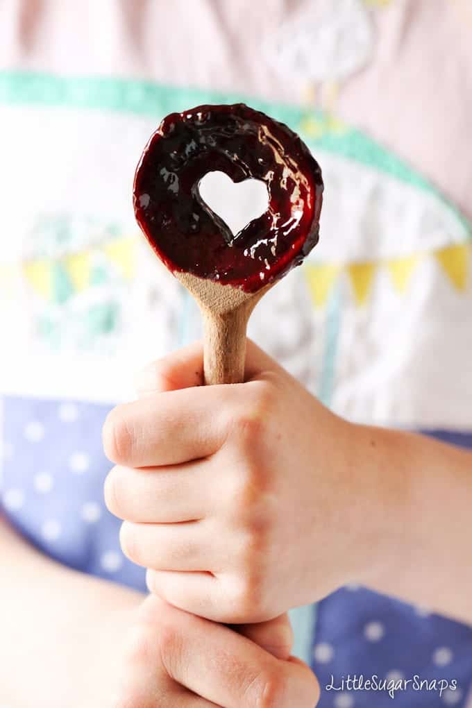 Child holding a wooden spoon with fruit sauce on it.