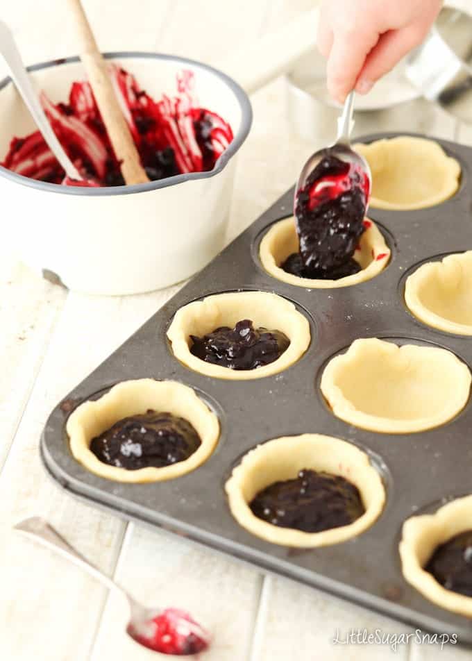 Child spooning fruit sauce into pastry cases.