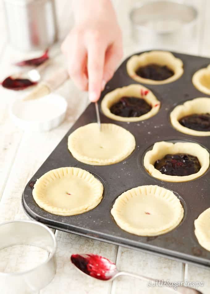 Child scoring the lids of small blackcurrant pies with a knife.