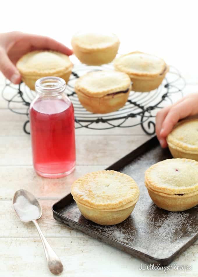 Children picking up small Blackcurrant Pies from baking sheets