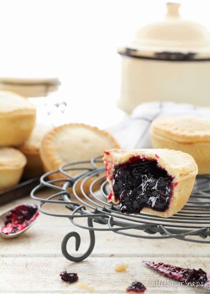 Blackcurrant pies on a wire rack - one is cut open.