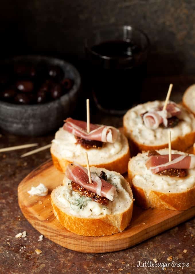 Fig, prosciutto and gorgonzola crostini on a wooden board.