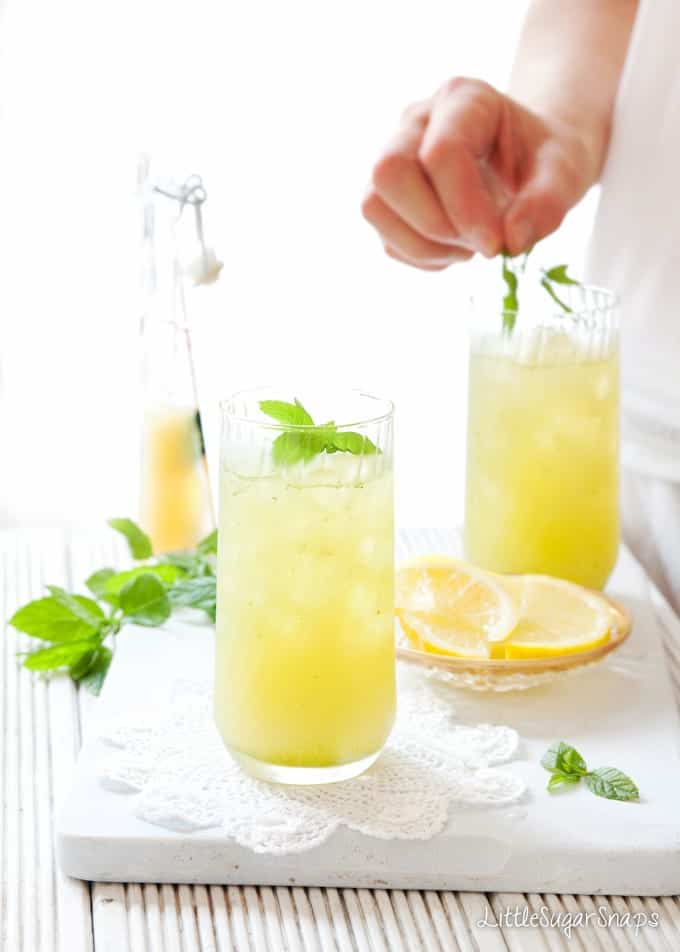 person adding mint leaves to glasses of Apple Lemon & Mint Fruit Cooler.