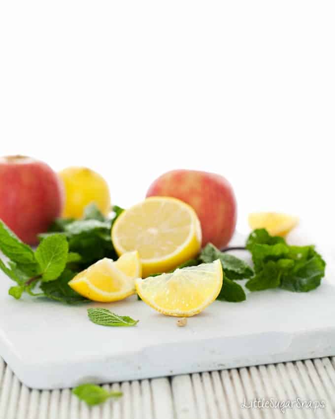 Ingredients on a board: apples, mint and lemons.