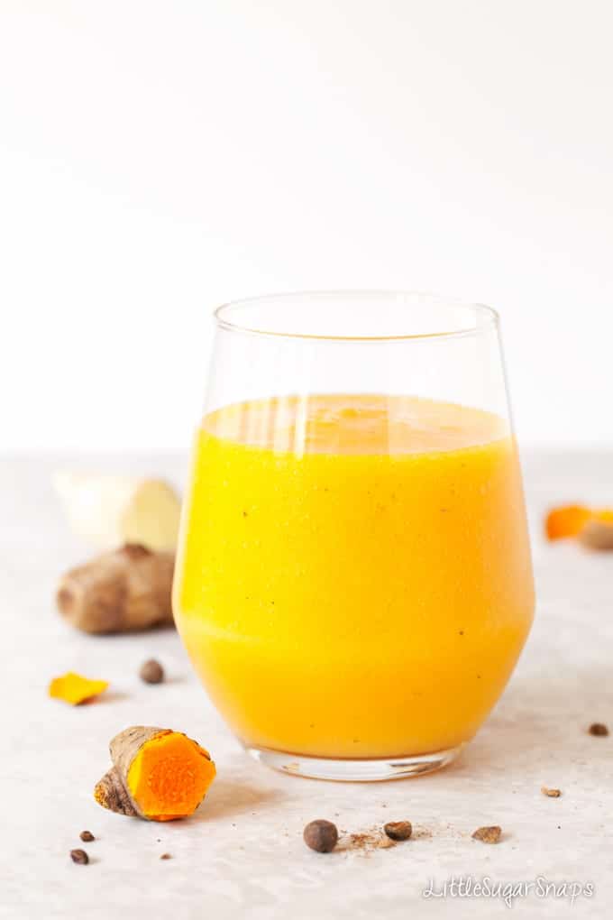 A glass of a yellow Turmeric Smoothie with fresh turmeric alongside.