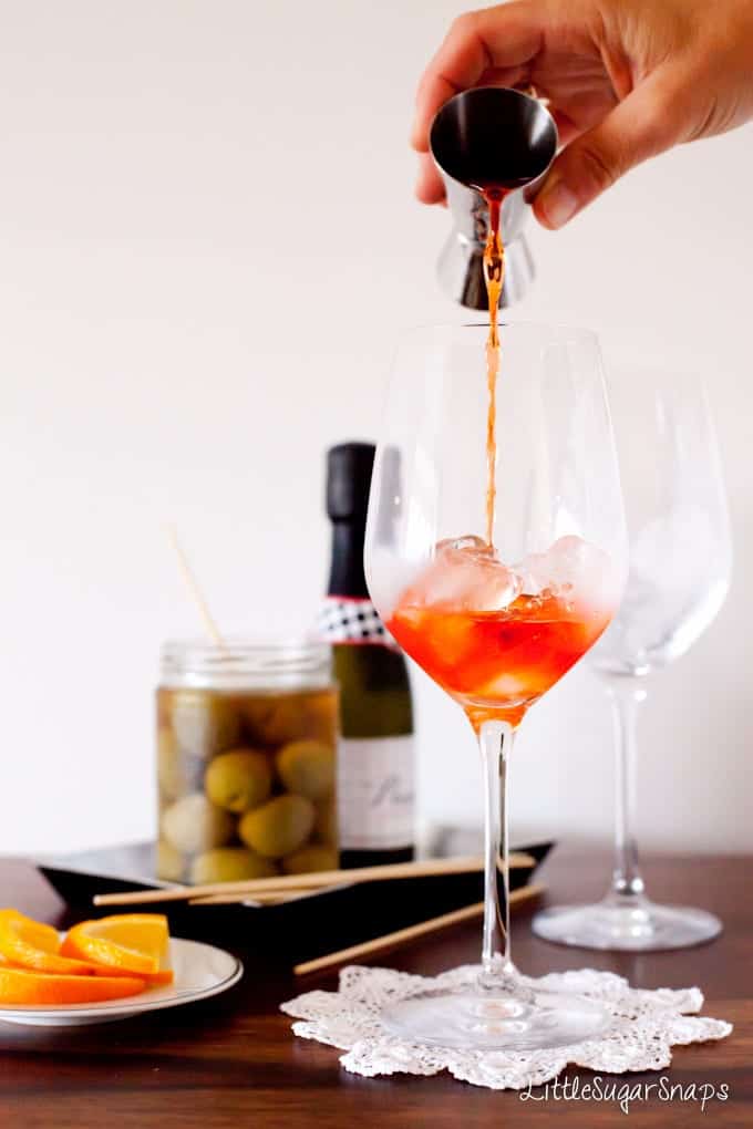 person pouring Aperol into a glass filled with ice.