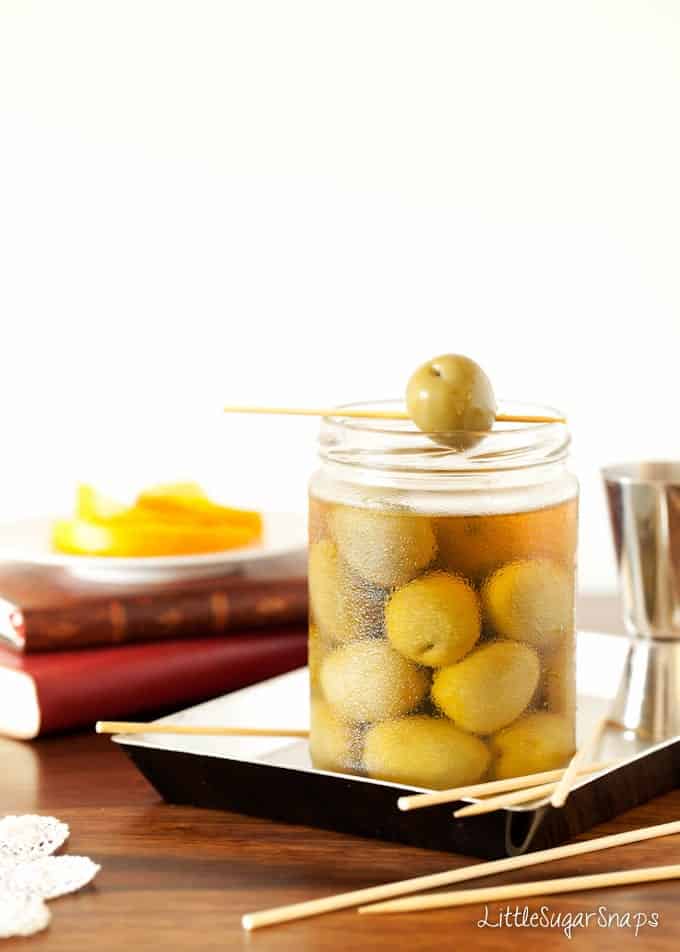 A jar of green olives with one resting on top.