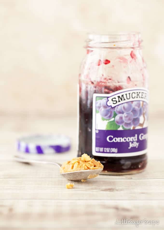 Open jar of grape jelly with peanut butter on a spoon alongside