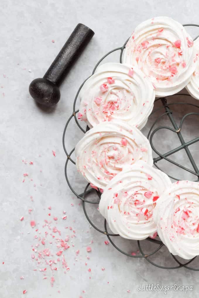 Circles of meringue on a wire rack. They are topped with candy cane pieces.