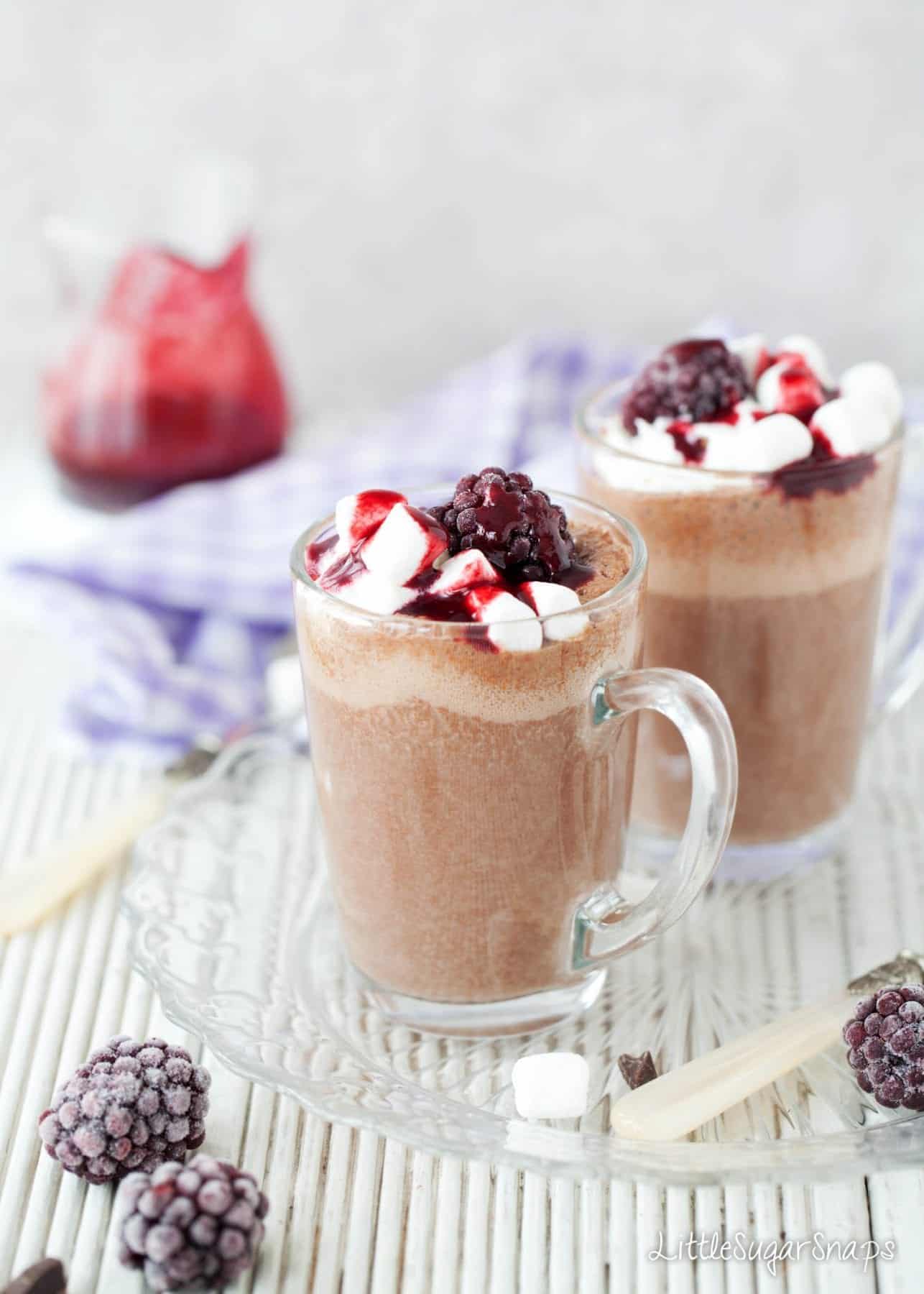 Glasses of frothy Hot Chocolate topped with cream and blackberry sauce
