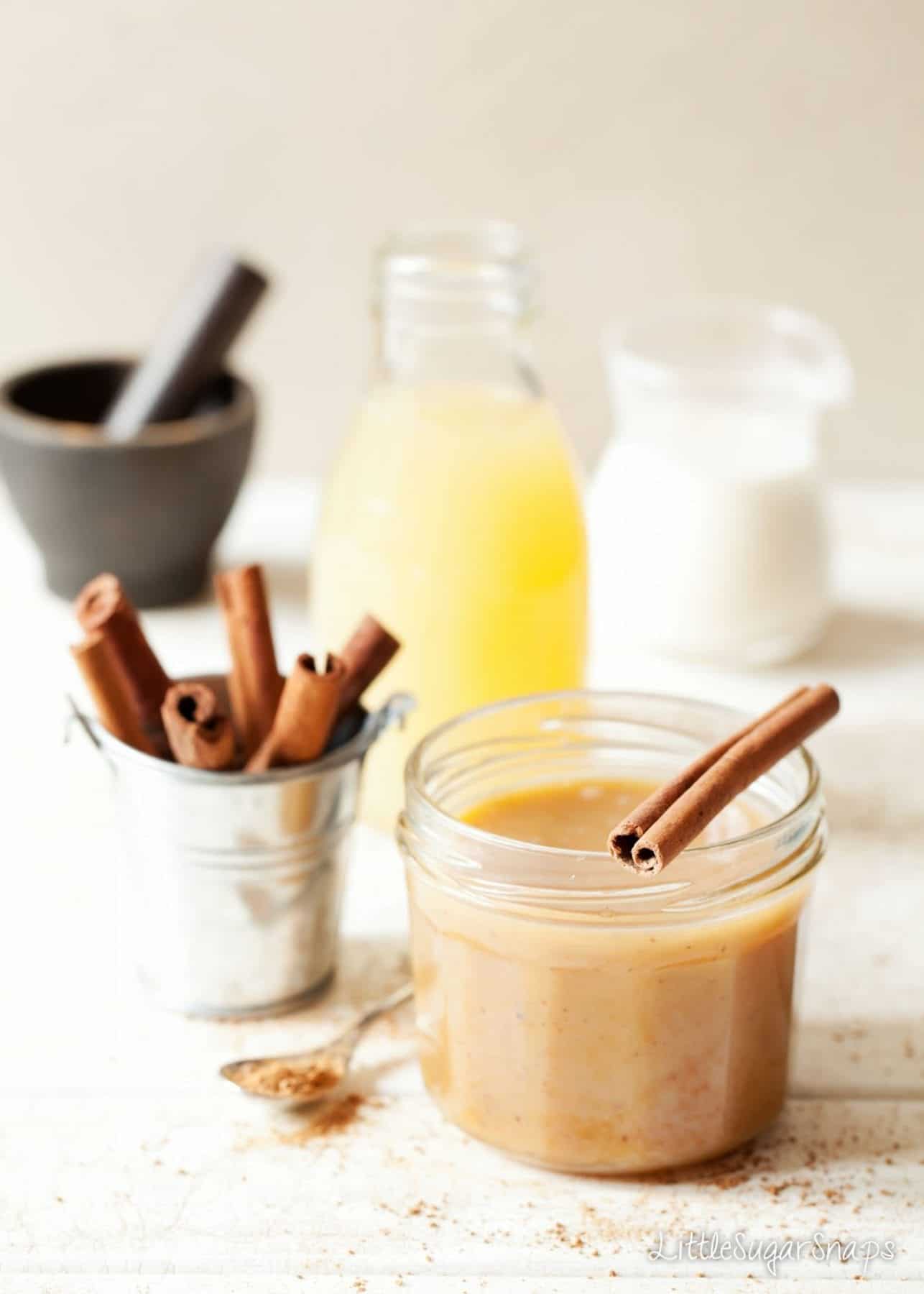 A jar of spreadable apple caramel sauce with cinnamon and apple juice alongside