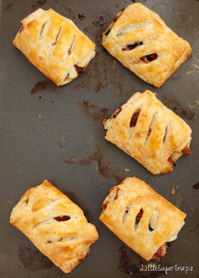 Five cooked savoury pastry rolls on a baking sheet