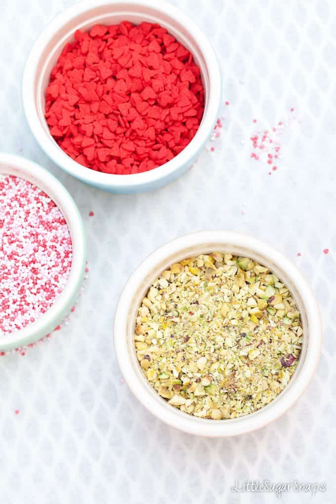 Multicoloured sprinkles, red heart sprinkles and chopped pistachio in bowls