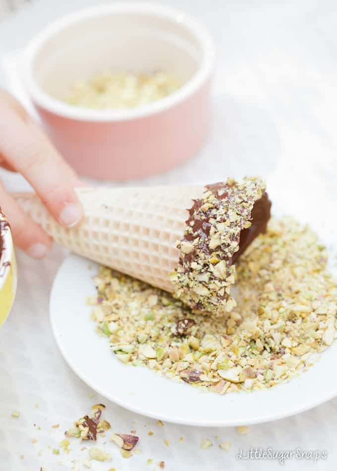 Child rolling a chocolate dipped waffle cone in pistachio nuts