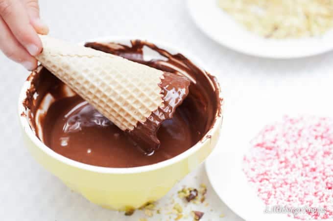 Child dipping the edge of a waffle cone into melted chocolate