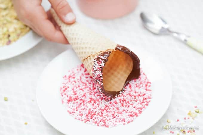 Child covering a chocolate dipped waffle cone into colourful sprinkles