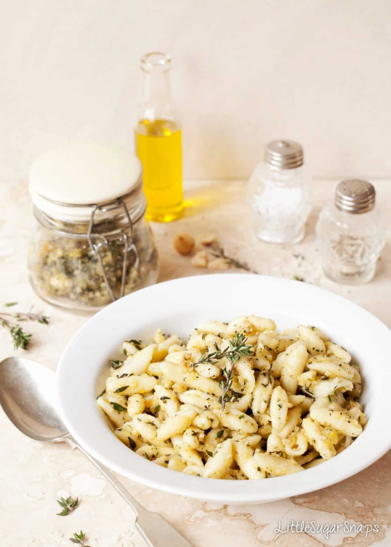 A bowl of pesto covered pasta alongside a jar of homemade pesto.