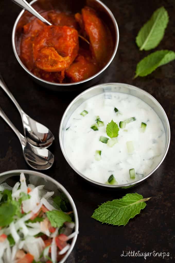 Bowls of raita, onion salad and mango chutney