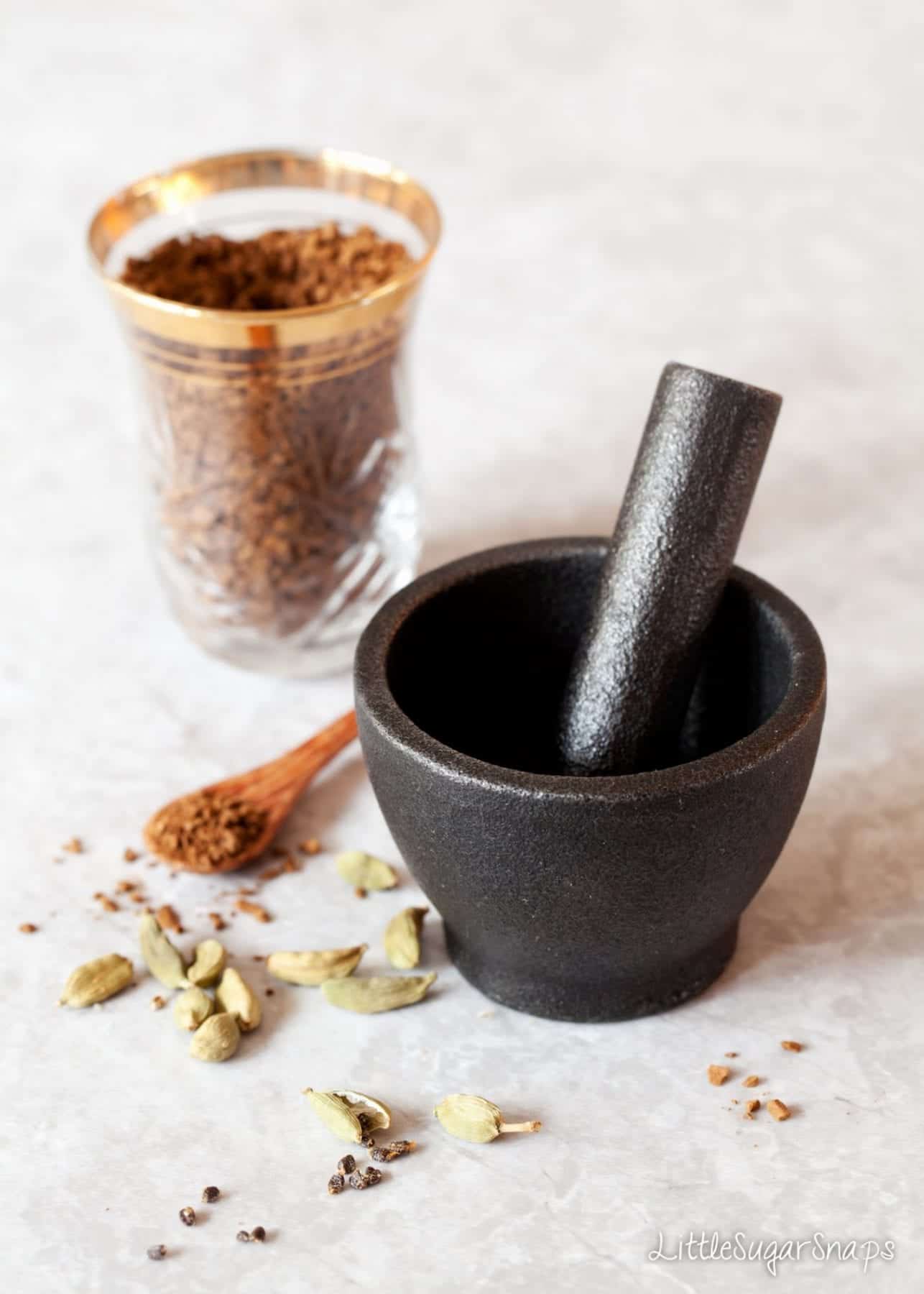 a black pestle and mortar with green cardamon in shot.