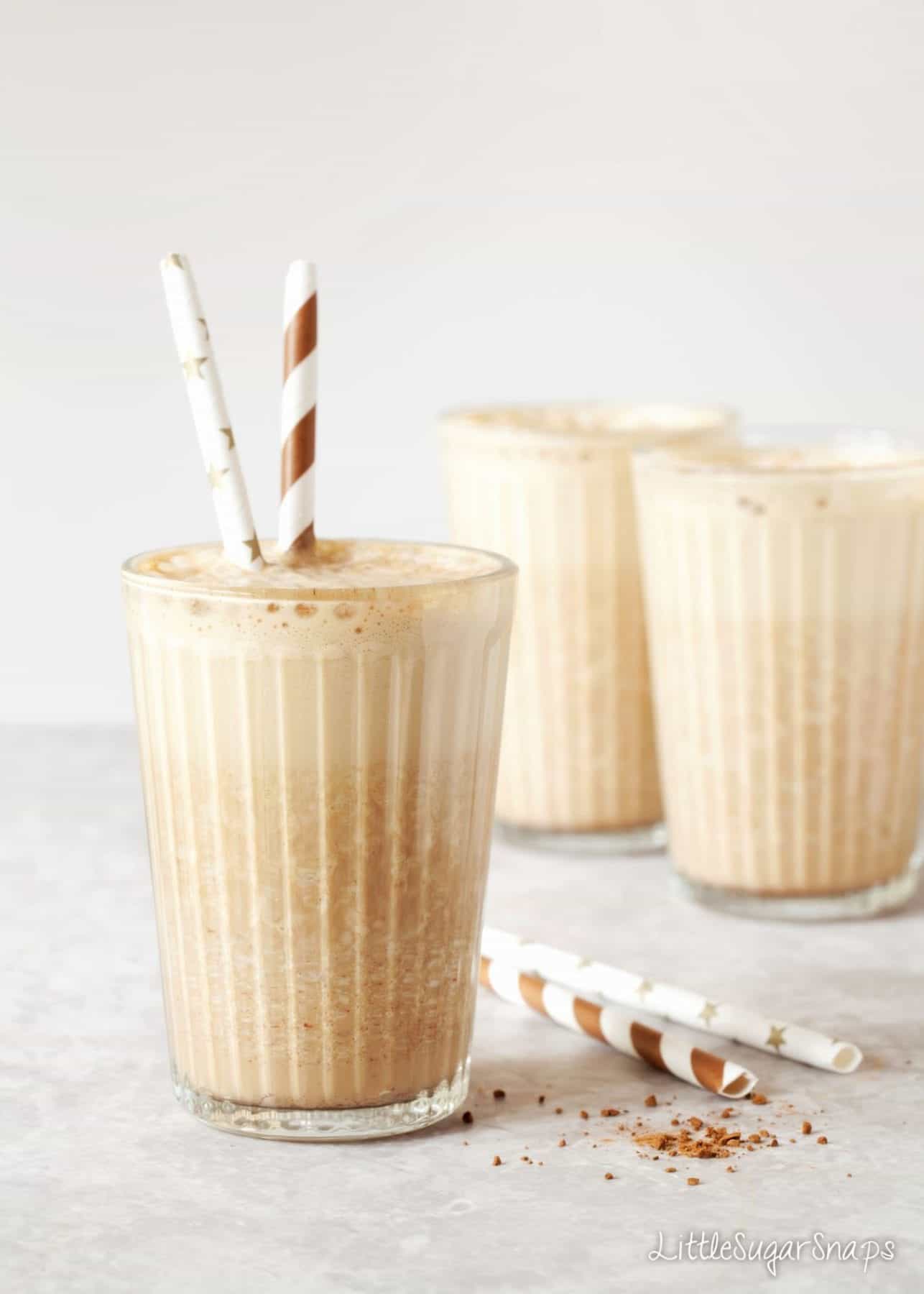Coffee milkshake in tall glasses with paper straw in them.